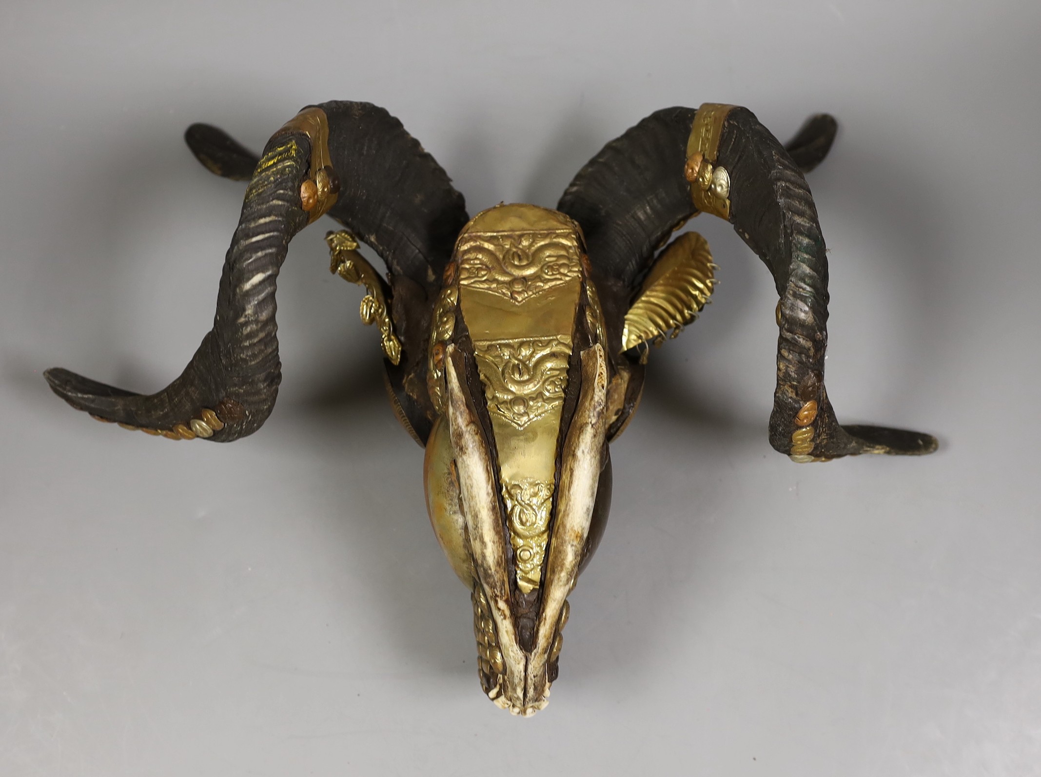 A Buddhist decorated ram's skull with brass decor, 20cm tall